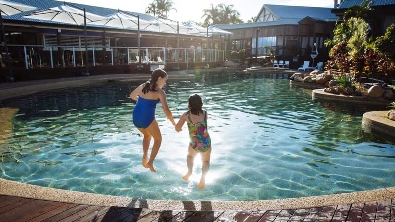 Two girls leap into a sparkling pool at Mercure Hotel Townsville, enjoying a playful summer moment