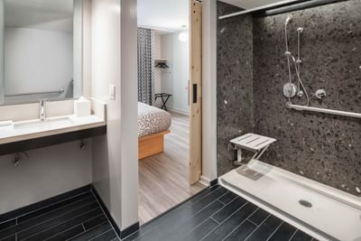 ADA King Comfy Room bathroom, with a roll-in shower and dark textured tile by the floating vanity at Hotel Keen