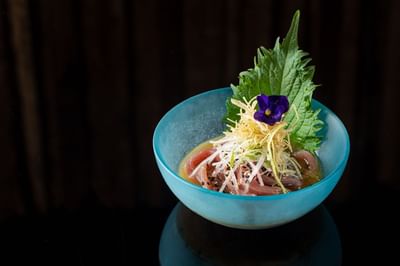 Blue bowl featuring fresh sashimi topped with shredded vegetables and herbs at The Kitchens