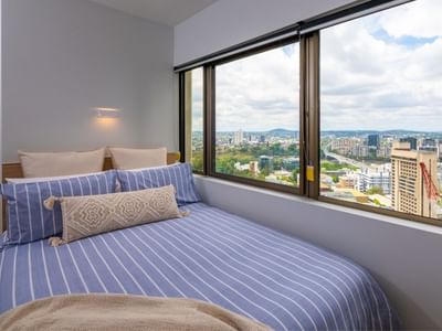 Blue bed with pillows and blankets in a bedroom with large window at UniLodge Brisbane City.