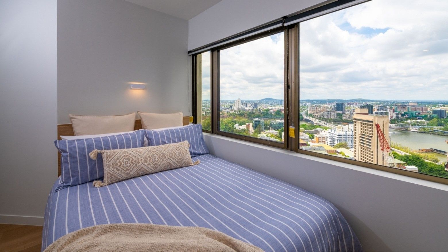Blue bed with pillows and blankets in a bedroom with large window at UniLodge Brisbane City.