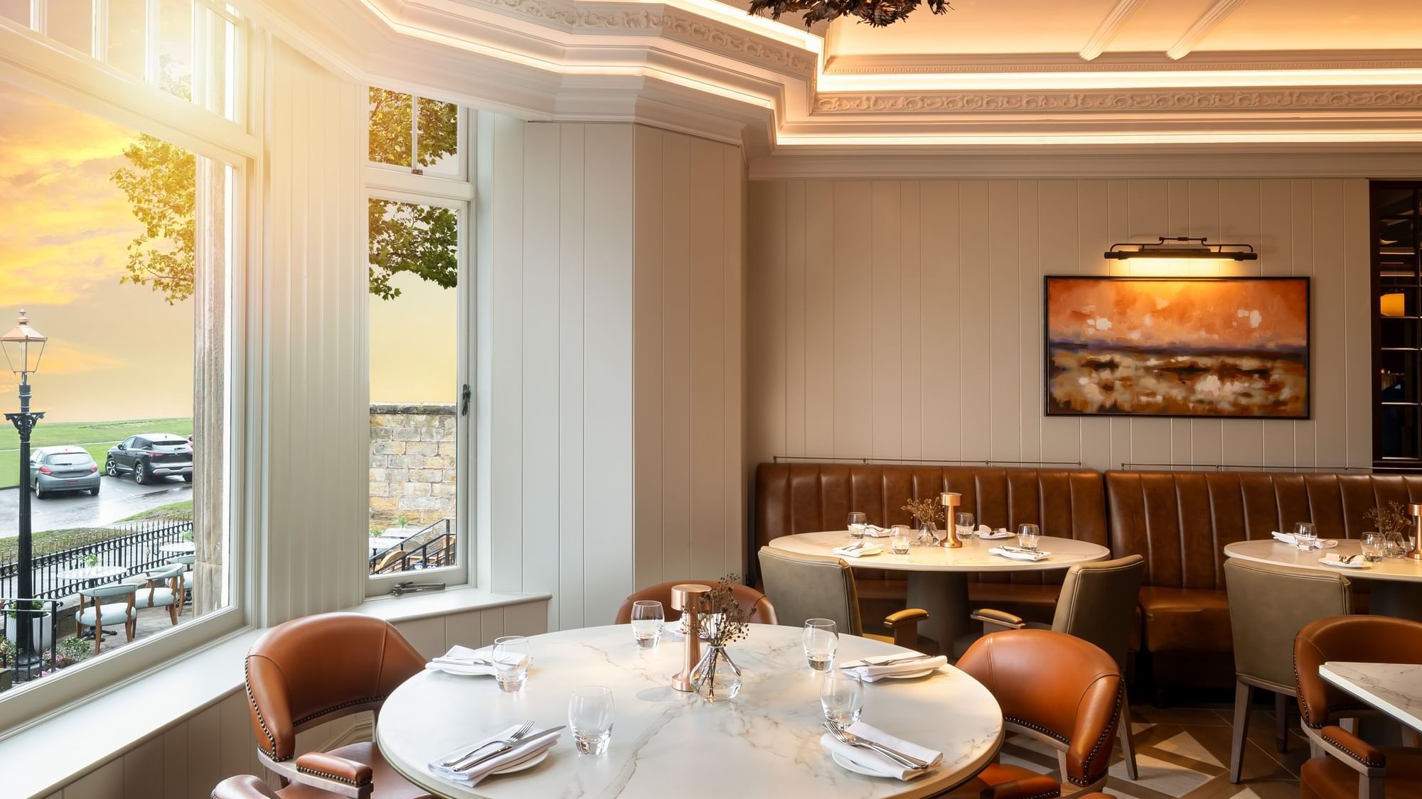 The Board Room with round tables, brown leather banquettes, and large windows with a sunset view at Seaton House