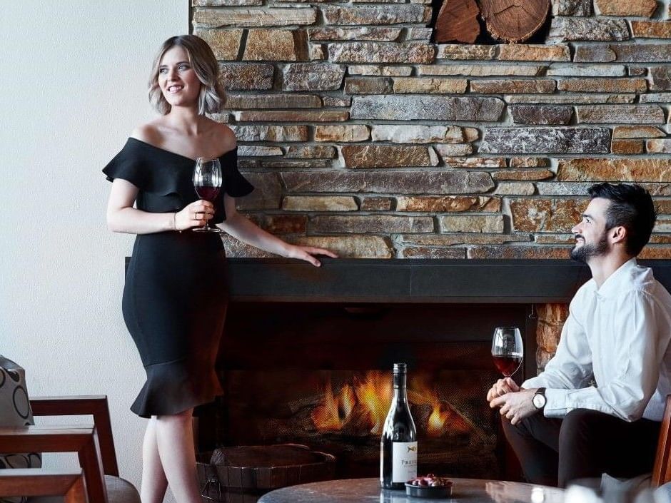 Couple enjoying red wine by a cozy stone fireplace in an elegant indoor setting during winter season