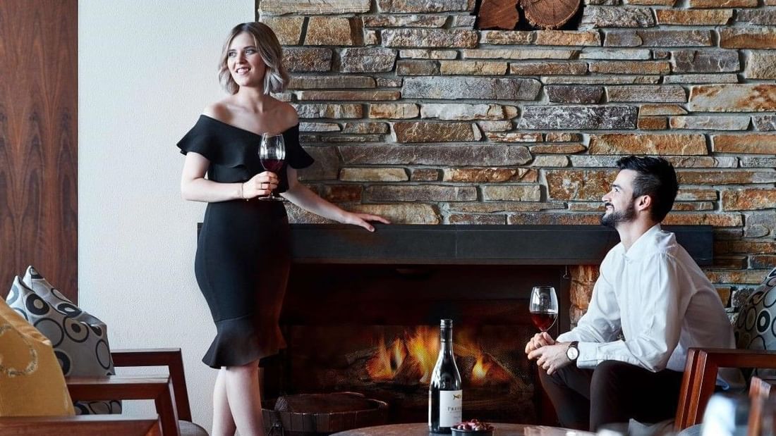 Couple enjoying red wine by a cozy stone fireplace in an elegant indoor setting during winter season