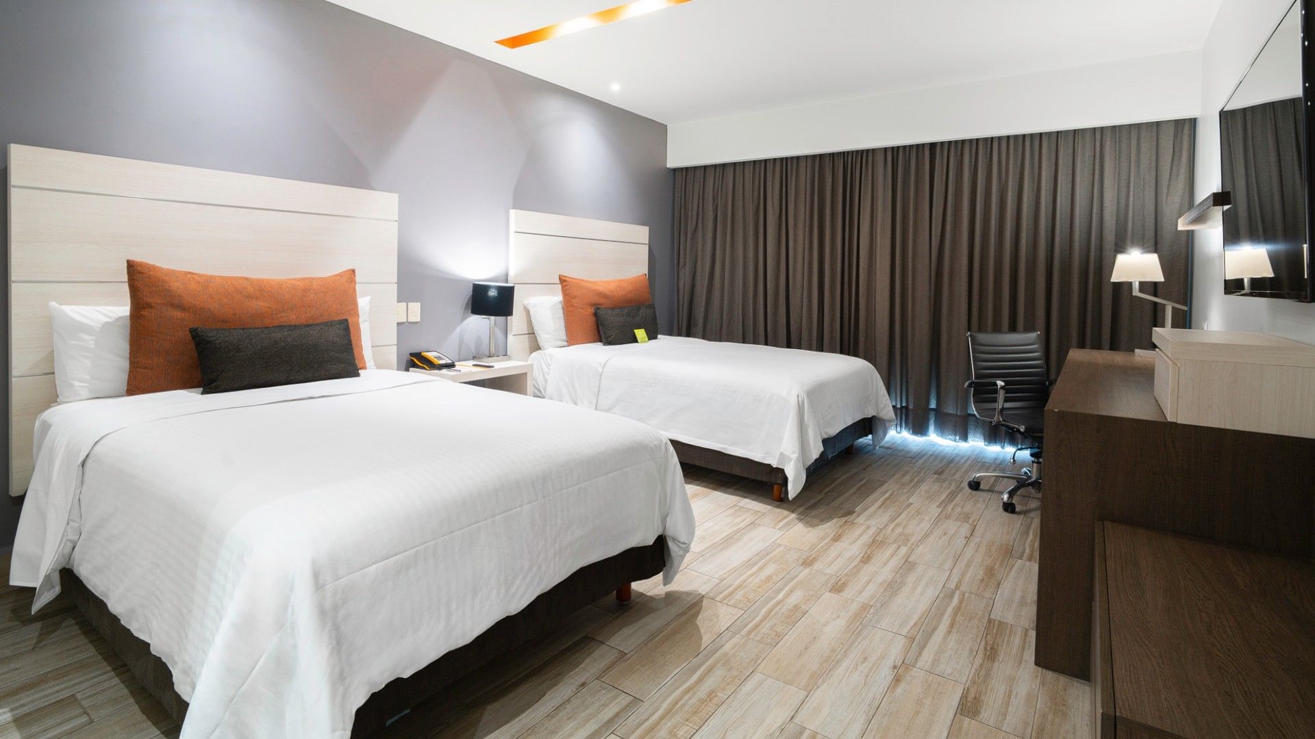 Two double deluxe beds with white linens and orange pillows at Real Inn Perinorte in Tlalnepantla.