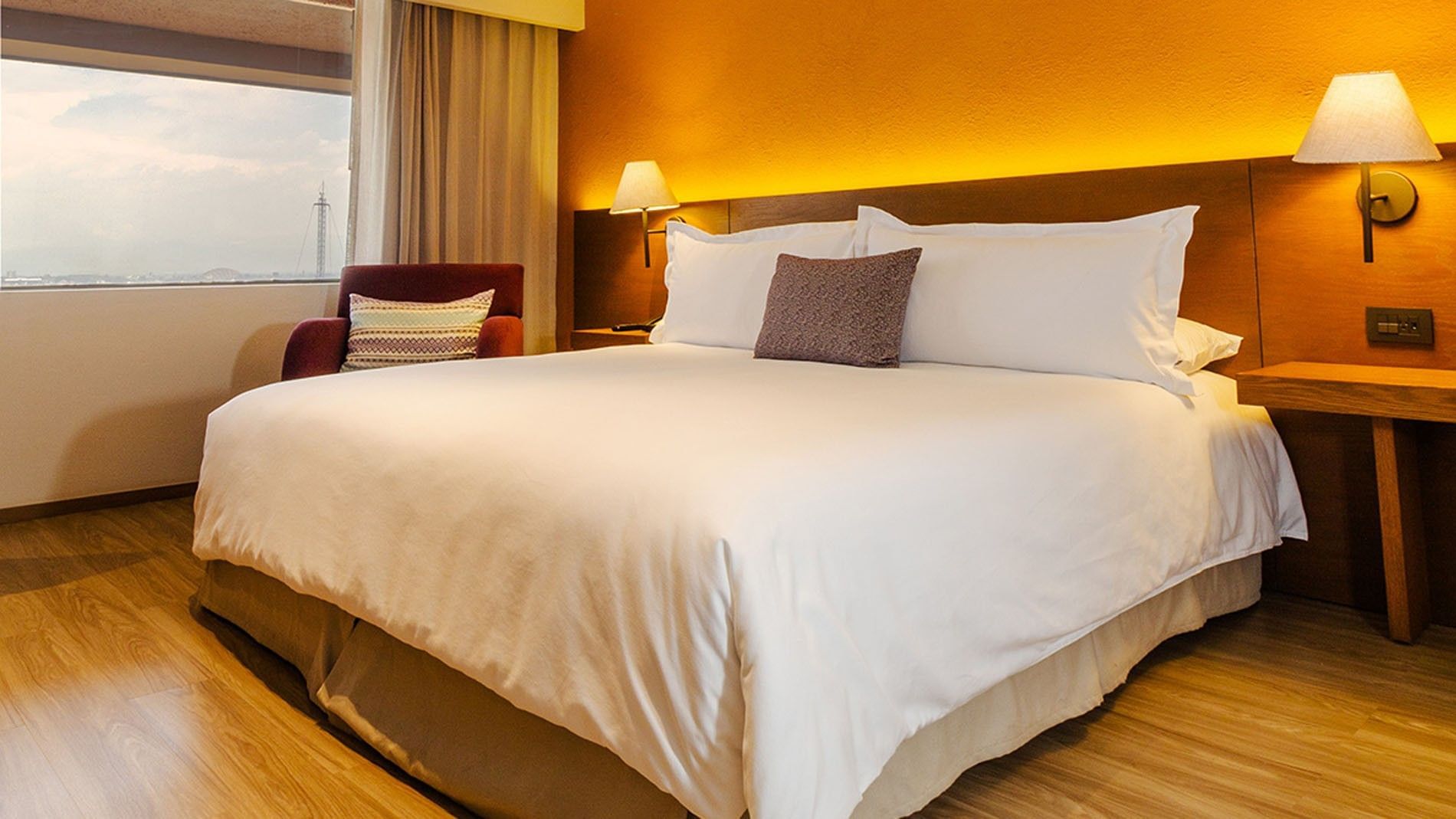 Bed with white linens and couch by the window in King Deluxe Superior at Camino Real Aeropuerto Mexico