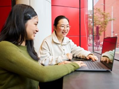 Two residents working on a laptop with a streetscape view in the background at Student Living D2.