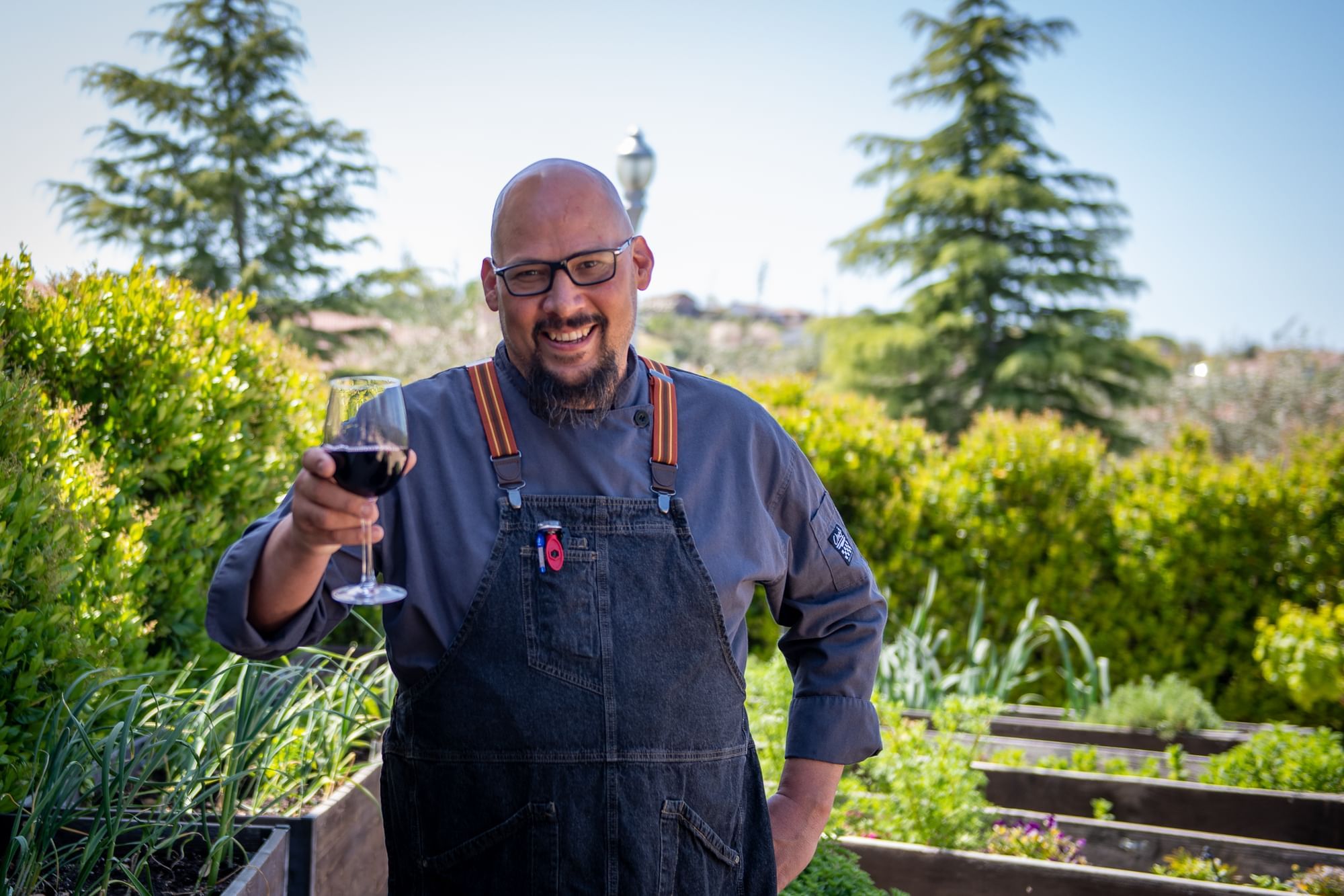 A man holding a wine glass in right hand standing in front of garden