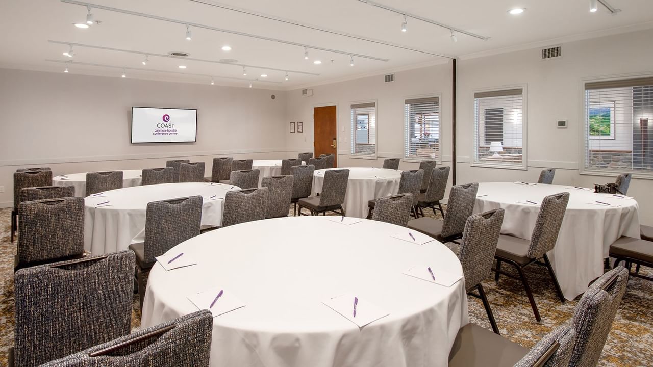 A conference room with round tables, chairs, a large screen, and a carpeted floor.