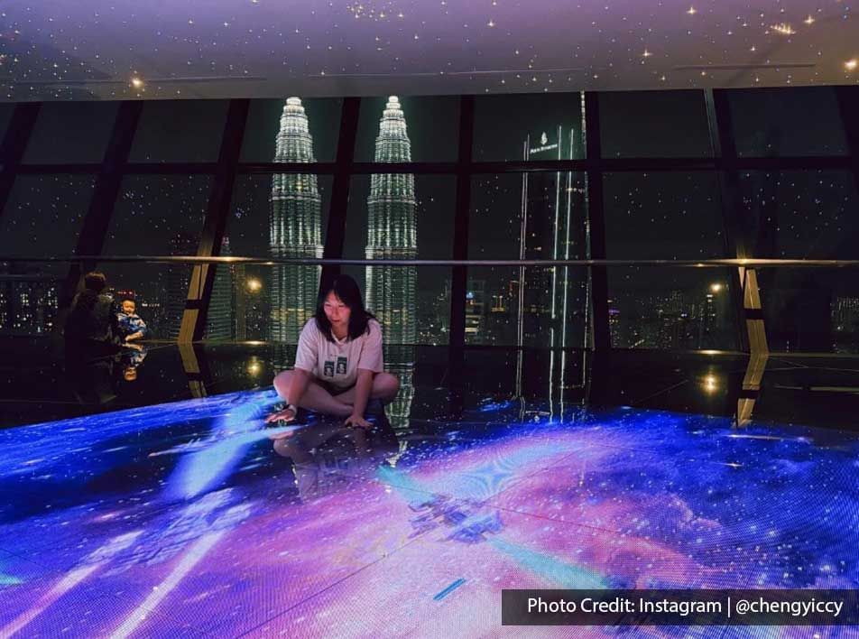 A woman sitting on the brightly illuminated floor, with a view of the Petronas Twin Towers at Imperial Lexis Kuala Lumpur.