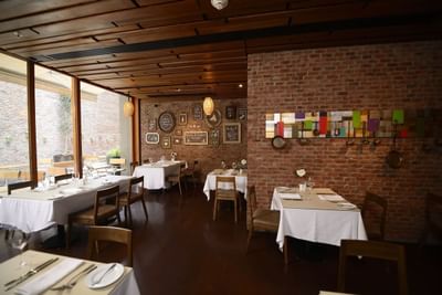 Mesas de comedor junto a muro de ladrillo bajo techo de madera en terraza de Fronterizo Restaurant en NOI Vitacura