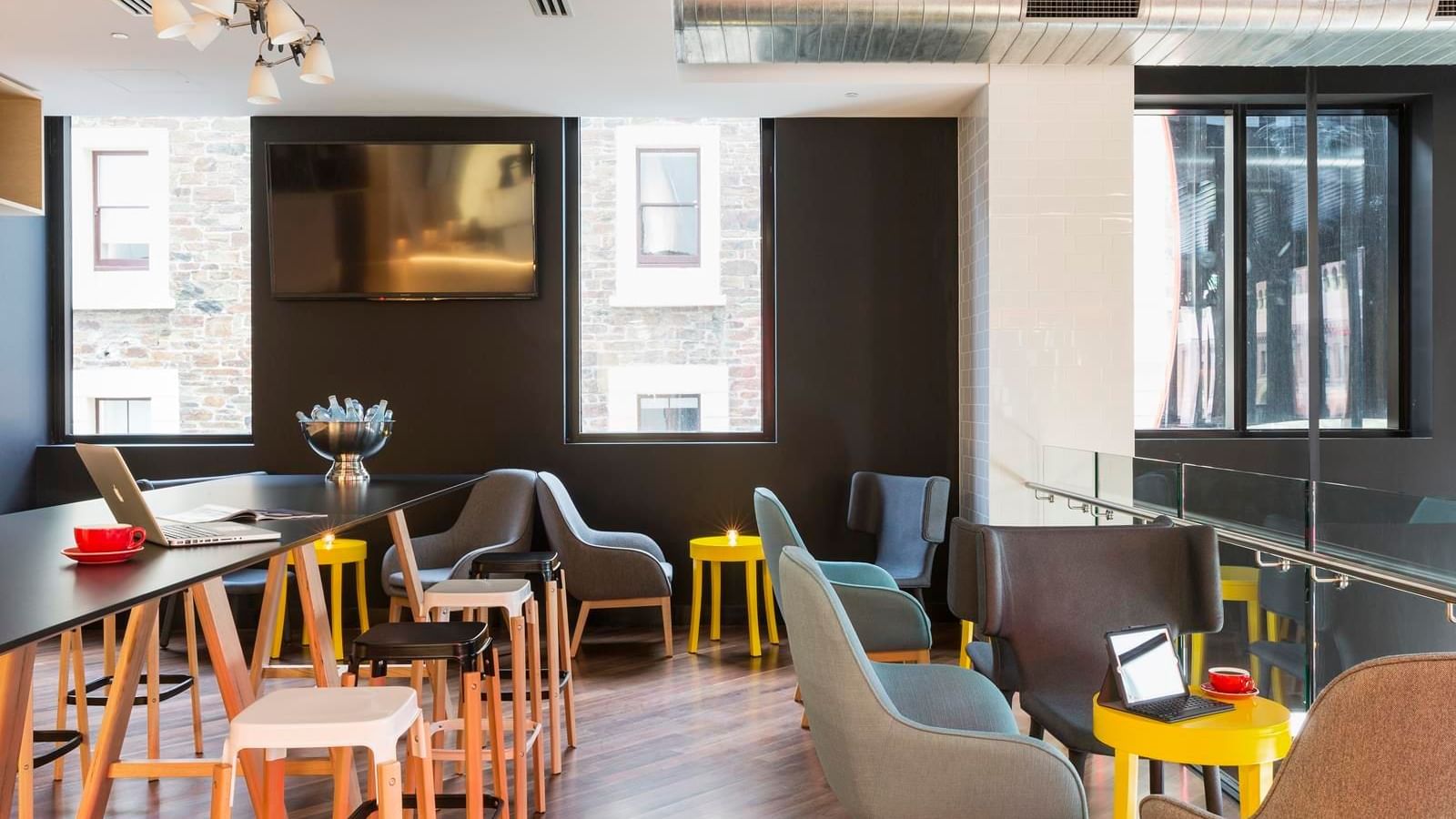 Level One Bar with modern seating, yellow tables, and a large communal desk at Ibis Adelaide