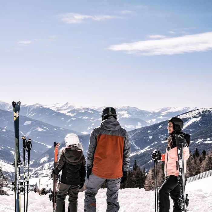 Drei Skifahrer mit Helmen und Skiern auf einem schneebedeckten Berg mit alpiner Aussicht.