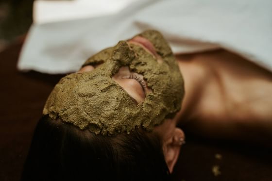 Woman relaxes with a green clay face mask, and lying on a bed in Pancha Kosha Himalayan Spa at Dwarika's Hotel Kathmandu