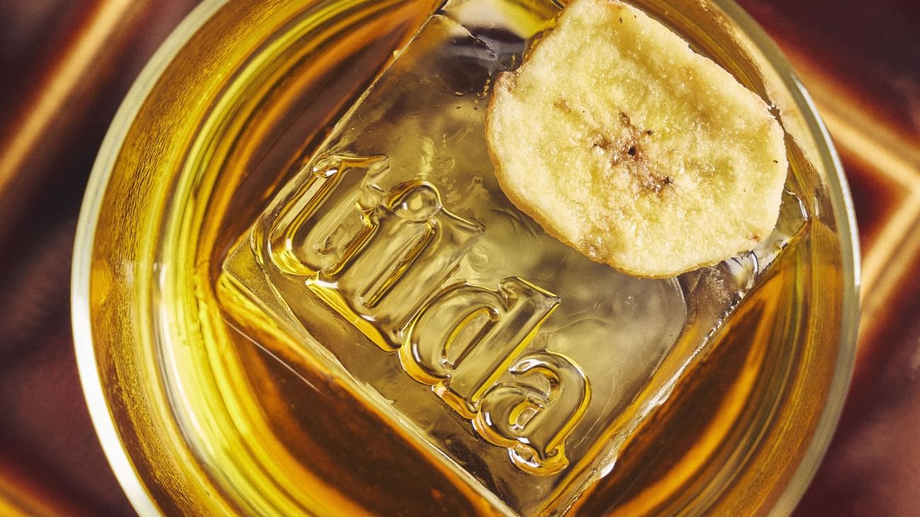 Glass of golden liquid with ice and a banana slice at Sofitel Sydney Wentworth.