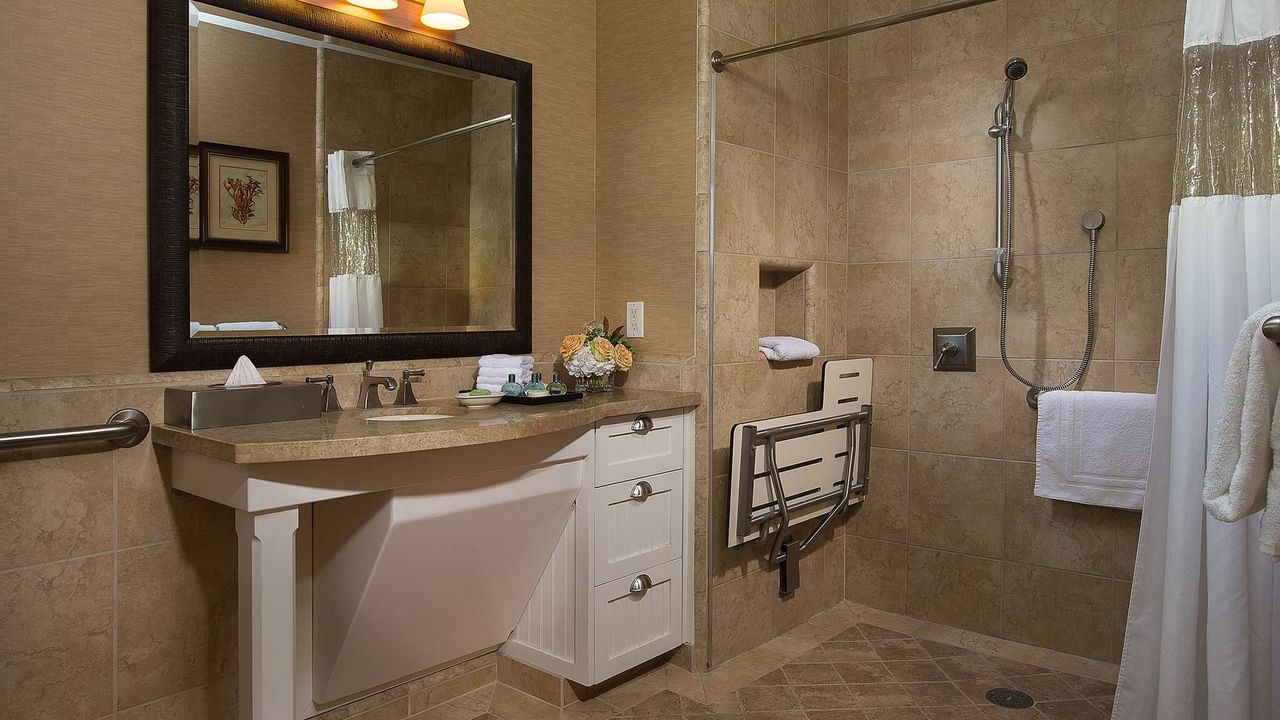 A handicap accessible bathroom with a sink, mirror, shower, and grab bar.