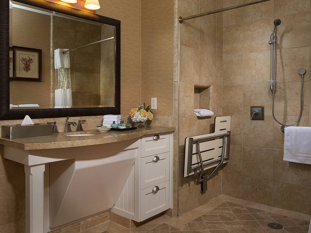 Accessible bathroom with vanity, mirror, white cabinets, shower with chair, and handrails.
