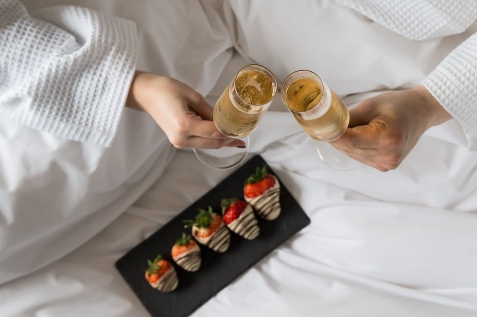 Couple toasting wine on a bed with Chocolate dipped strawberry plate at The May Fair Hotel