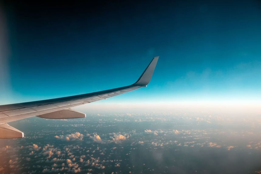 Airplane wing stretching above soft clouds under a deep blue sky during flight near Hotel Saint Clair in Chicago city