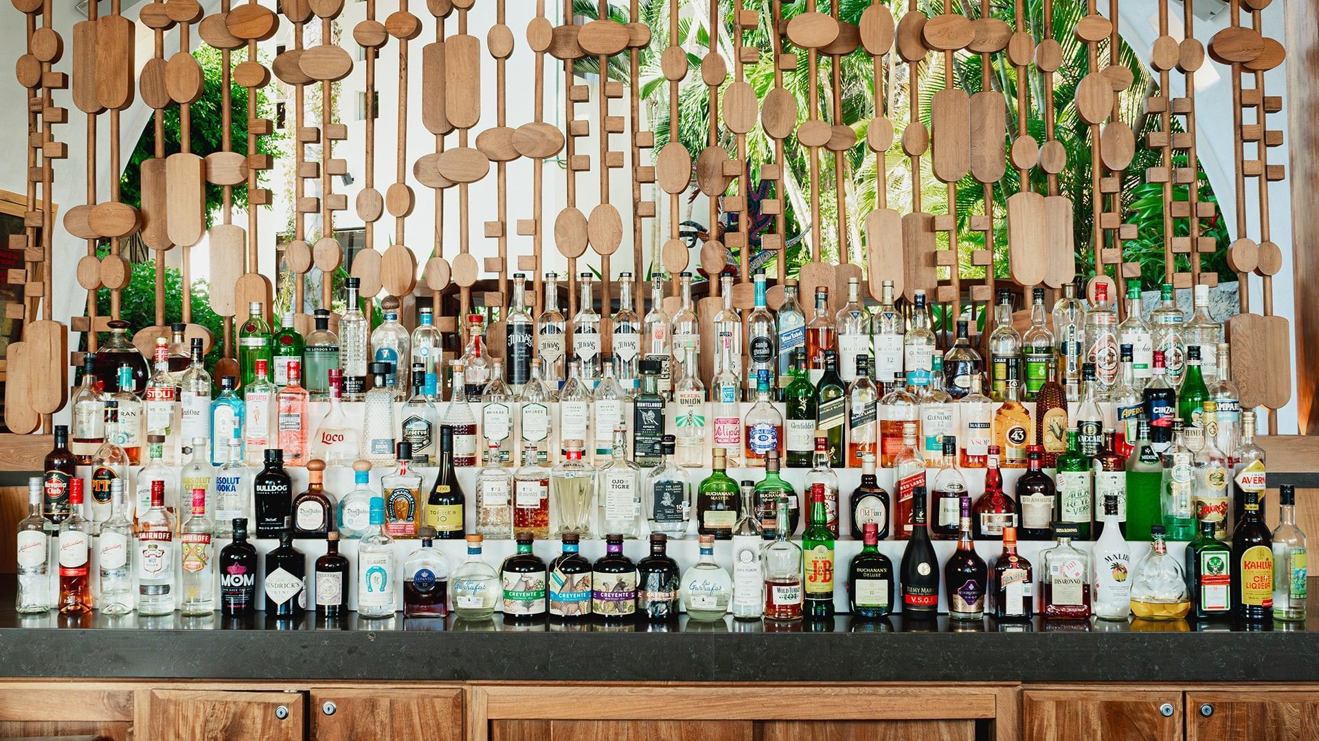 Liquor bottles on a bar shelf with artistic wooden decor in Bitza Lounge Bar at Camino Real Zaashila Huatulco
