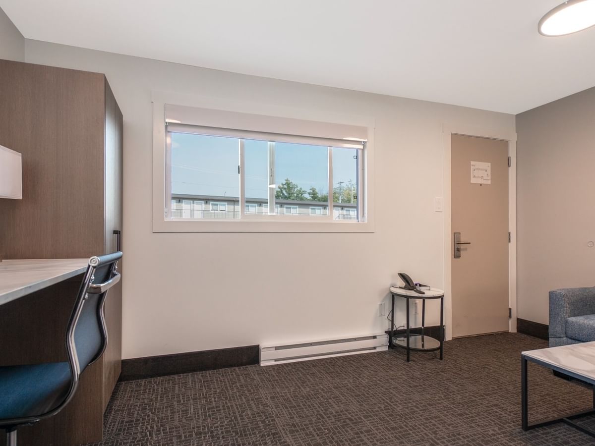 Modern hotel suite with couch, coffee table, desk, chair, window, and door.