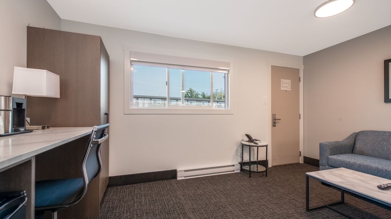 Modern hotel suite with couch, coffee table, desk, chair, window, and door.