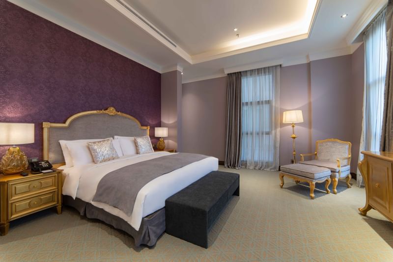 غرفة نوم فاخرة بسرير كبير وأثاث ذهبي وجدران أرجوانية ورمادية في Warwick Al Khobar