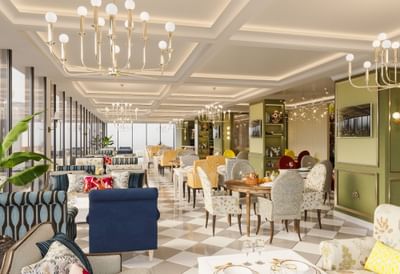 Patterned dining chairs by round wooden tables under gold chandeliers in The Tower View at Cantonal Hotel by Warwick Riyadh