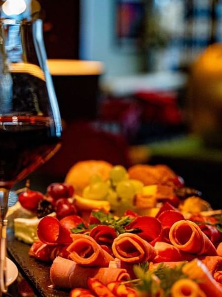 Glass of red wine by a slate board with rolled meats and grapes on a table in Bar “Le W” at Warwick Paris Champs Elysées