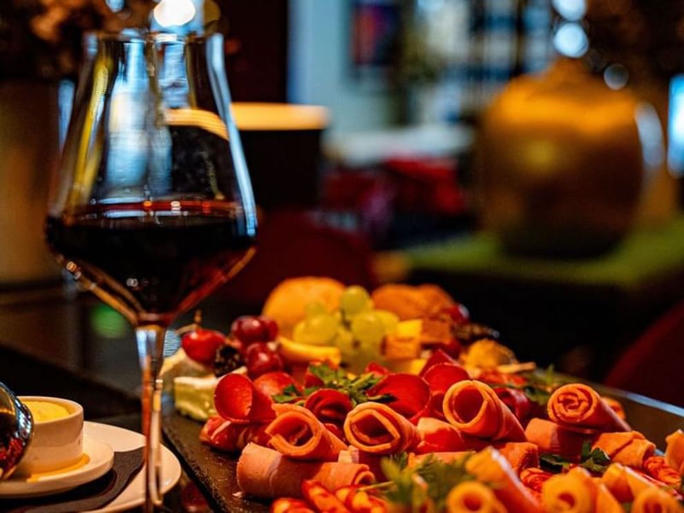 Glass of red wine by a slate board with rolled meats and grapes on a table in Bar “Le W” at Warwick Paris Champs Elysées