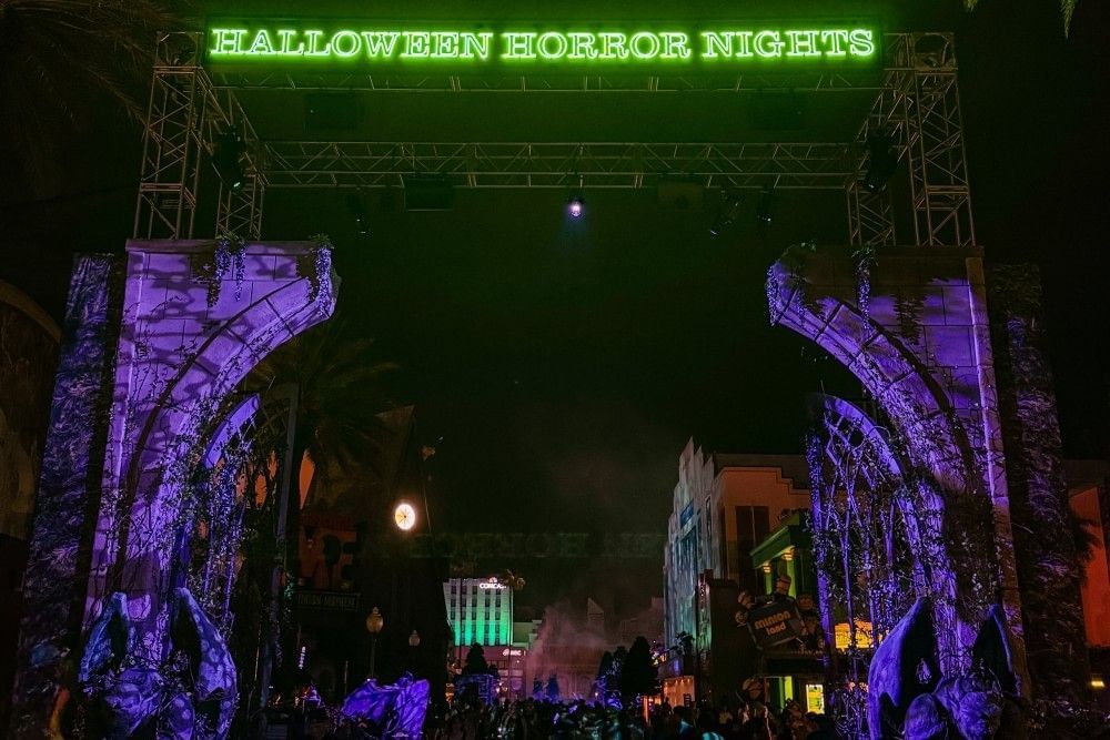 Dark scaffolding with eerie purple lighting and a glowing green sign that reads Halloween Horror Nights.