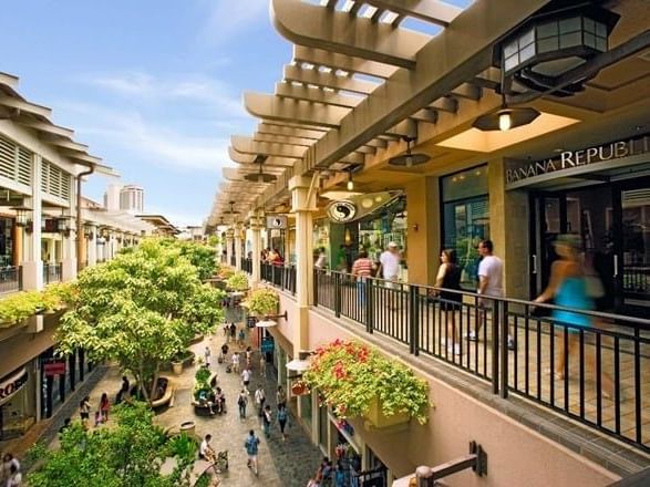 A bustling shopping mall filled with people walking and browsing various stores near Waikiki Resort Hotel