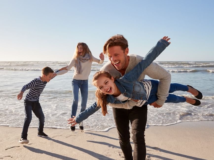 Family of four joyfully playing on the beach, with the father lifting a daughter.