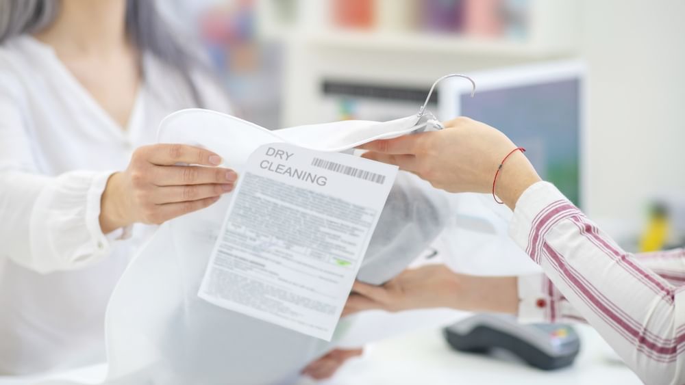 Guest handing dry cleaning in a protective cover to a staff member at The Capital Hotel, Apartments and Townhouse