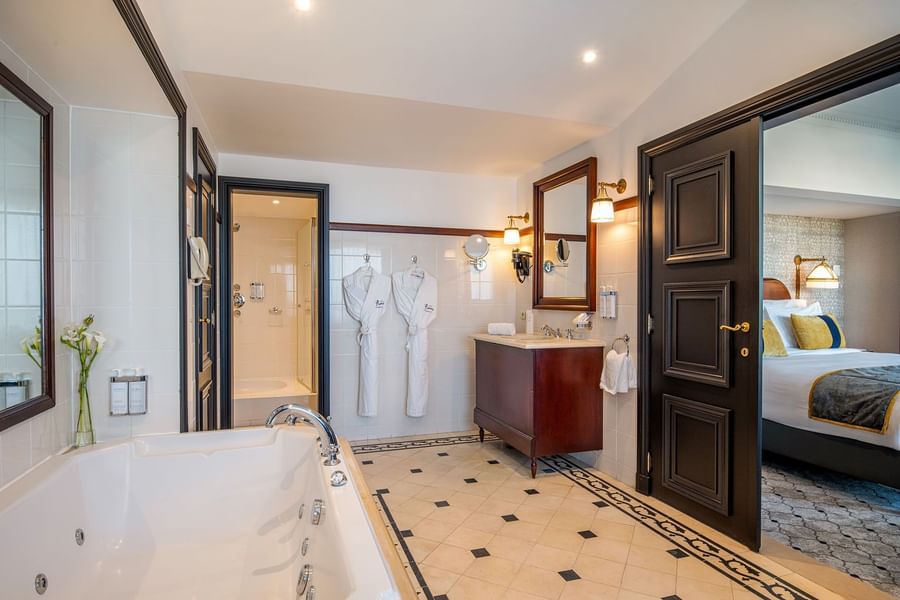 Barsey Suite bathroom soaking tub & white bathrobes hanging view into bedroom at Hotel Barsey by Warwick