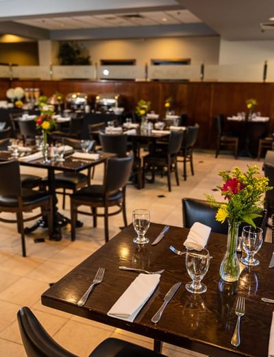 Natoma Bar & Grill dining area with dark wood tables, black chairs, and floral centerpieces at Lake Natoma Inn
