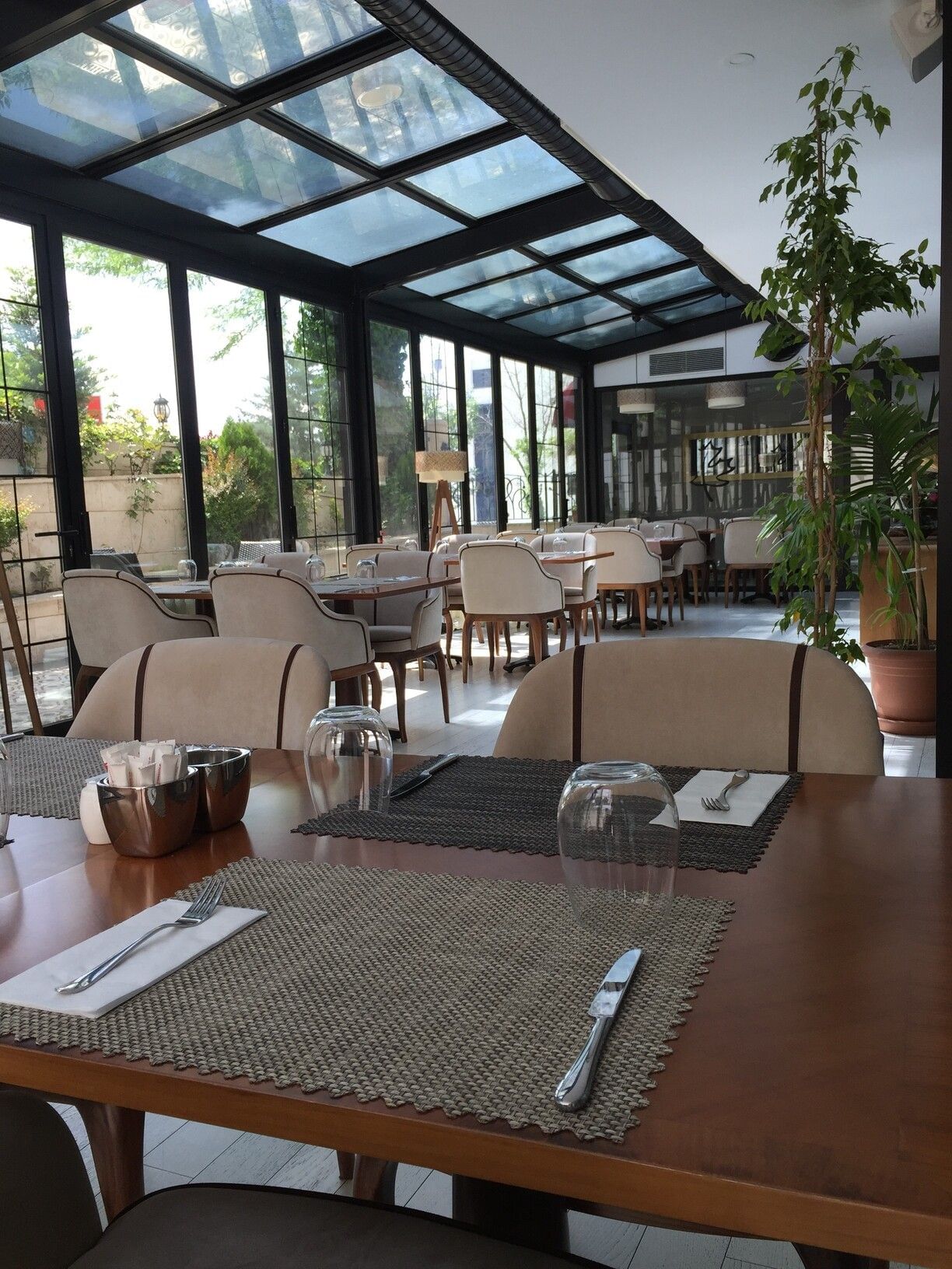 Maple Tree Restaurant with chairs by a wooden table under a glass canopy near potted plants at Warwick Ankara