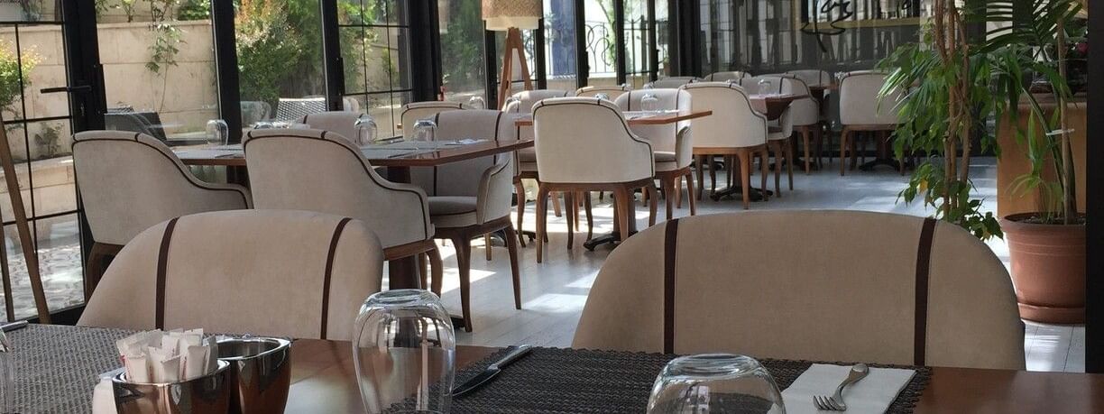 Maple Tree Restaurant with chairs by a wooden table under a glass canopy near potted plants at Warwick Ankara