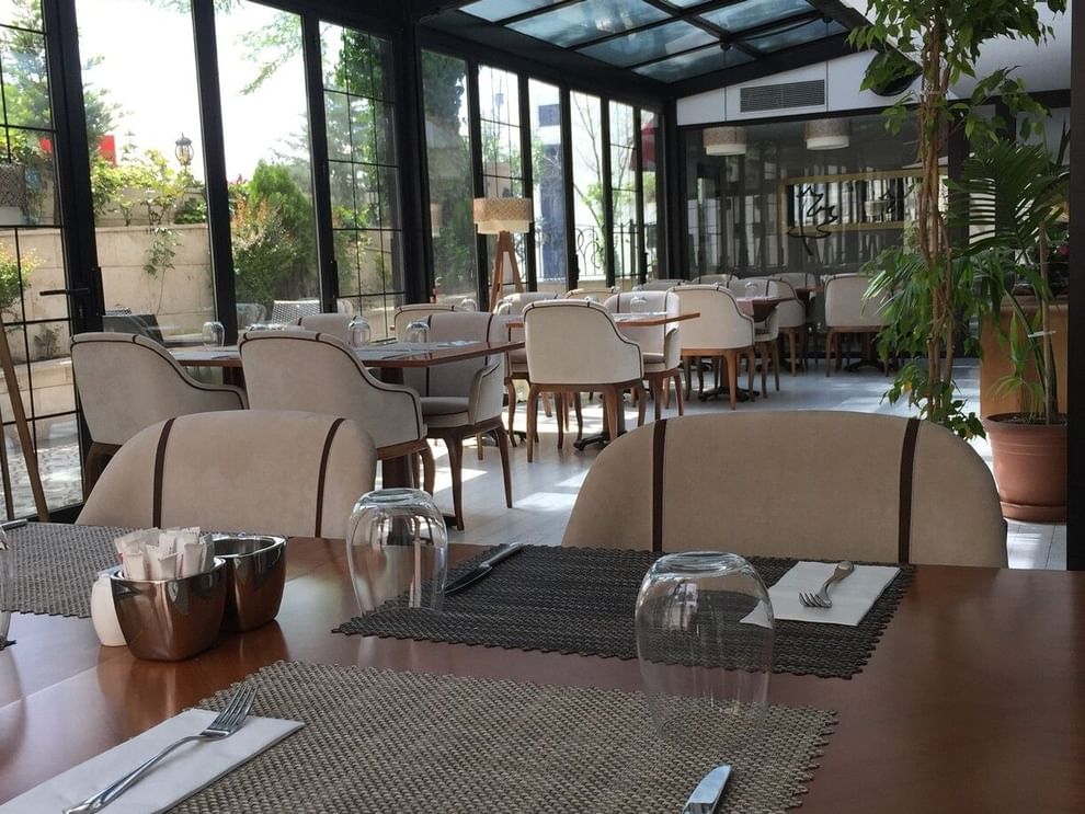 Maple Tree Restaurant with chairs by a wooden table under a glass canopy near potted plants at Warwick Ankara