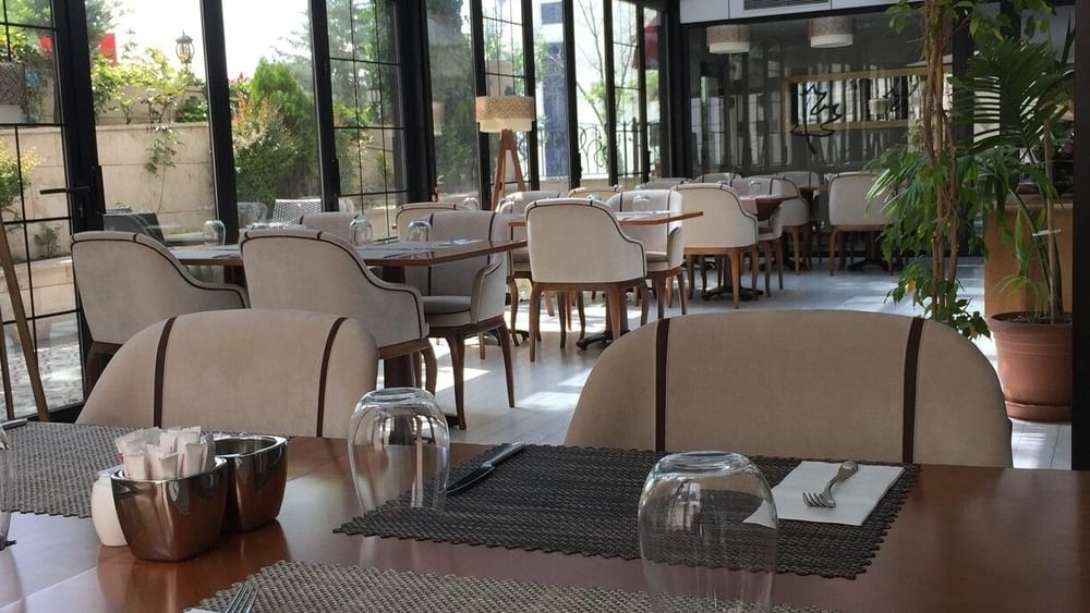 Maple Tree Restaurant with chairs by a wooden table under a glass canopy near potted plants at Warwick Ankara