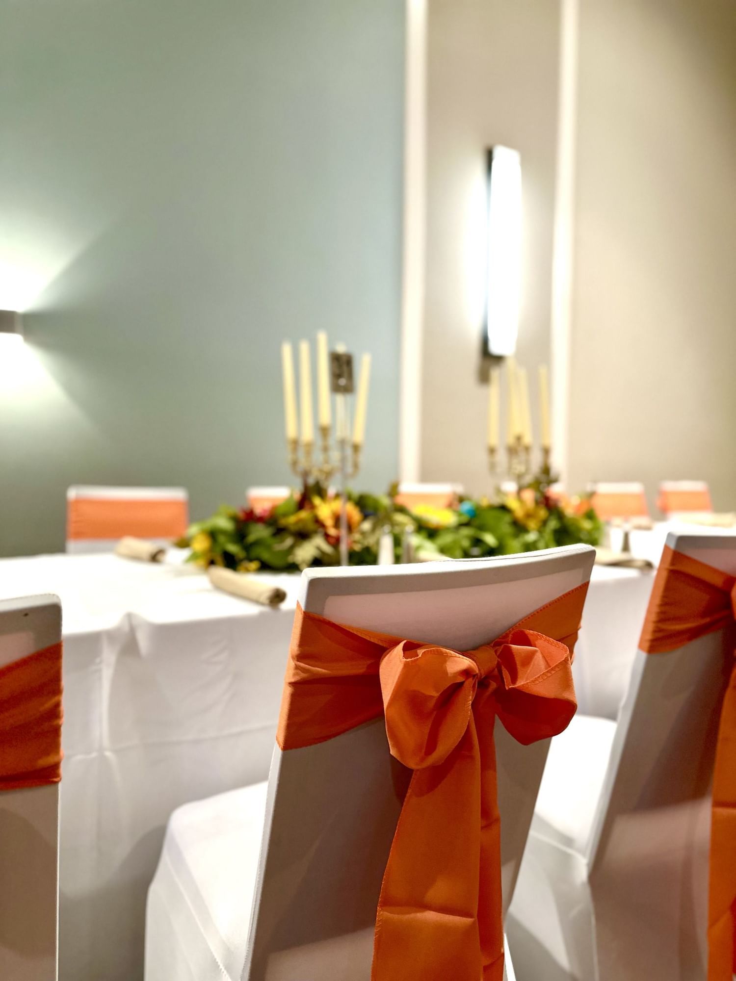 Chairs tied with orange ribbons at a long table dressed with candelabras and autumn flowers.