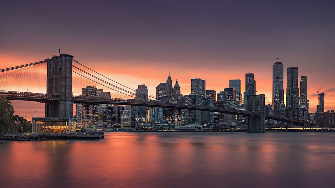 The Brooklyn Bridge and Manhattan skyline at sunset with vibrant orange and purple hues near Le Grand Hôtel des Thermes