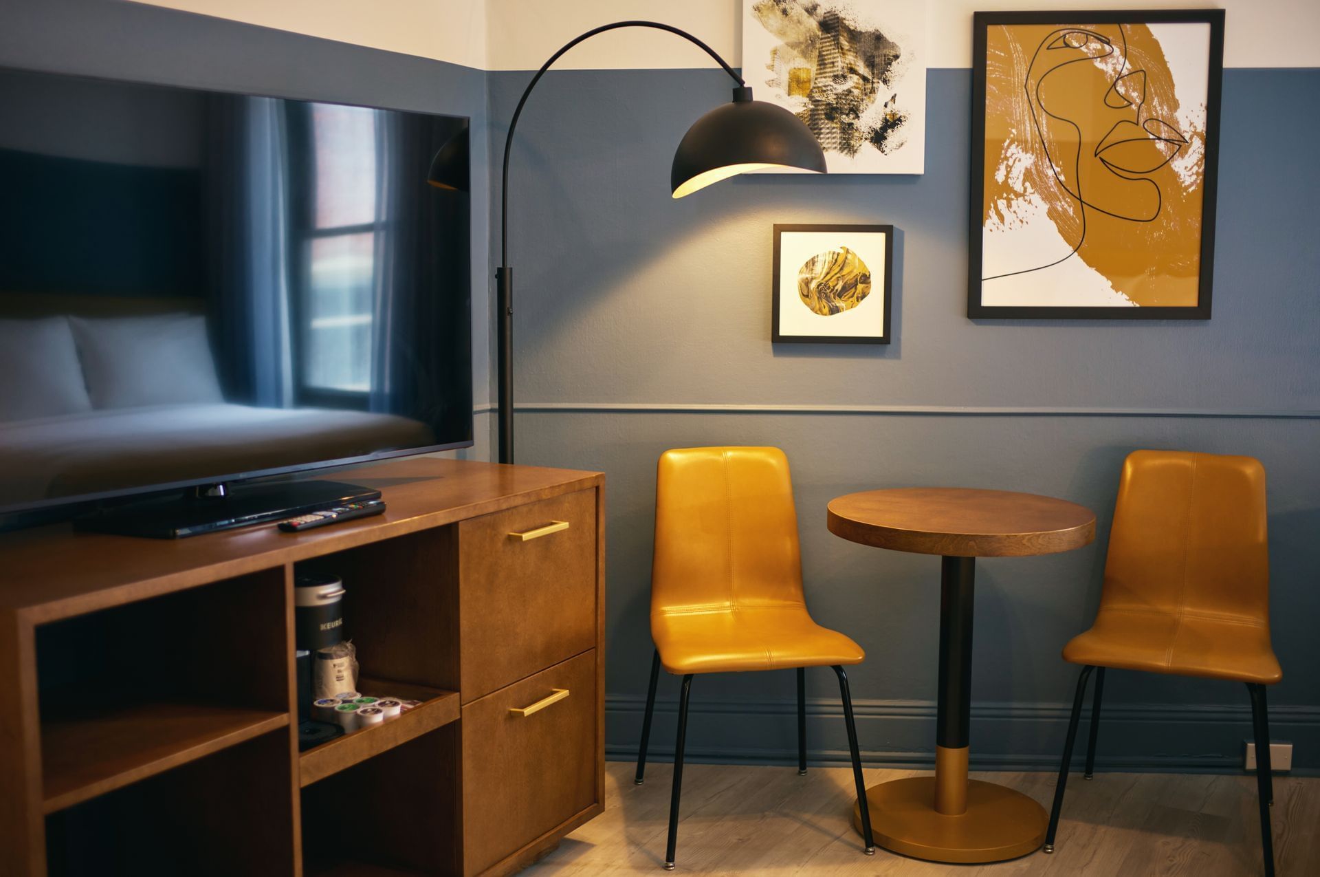 A hotel room with a TV, table, chairs, and artwork