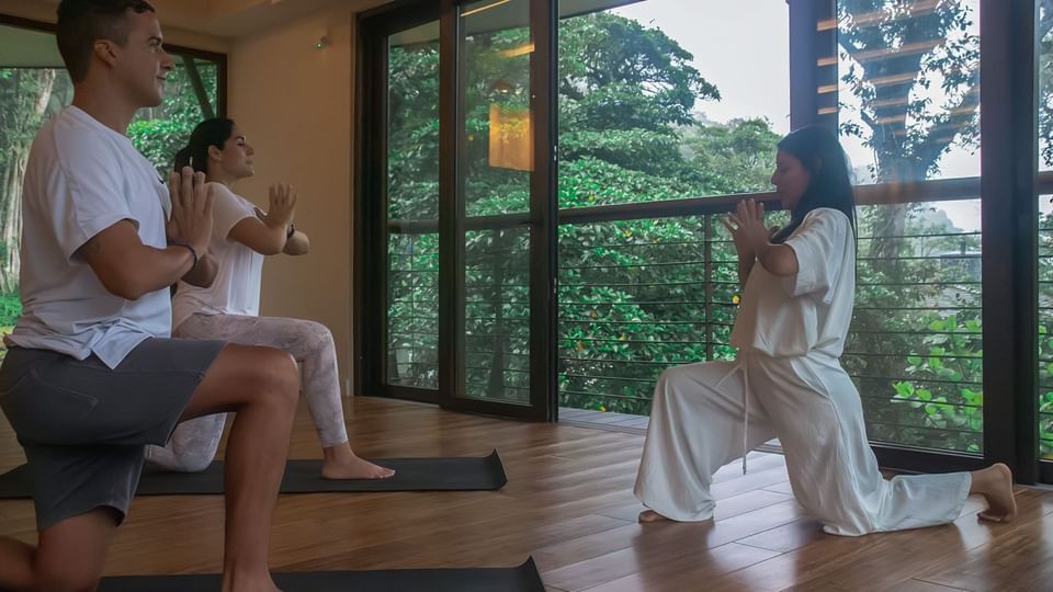 Three people doing yoga in Wellness Center with a forest view at El Silencio Lodge & Spa