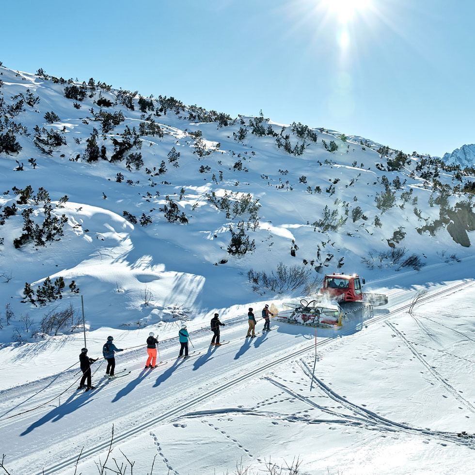 Sette sciatori e due veicoli trainano slitte su una pista innevata con sole splendente.