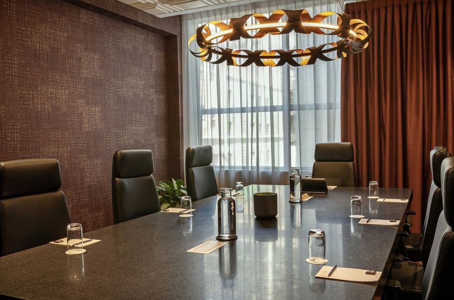 Leather chairs by a long stone table under a circular light fixture in Salon Du Président at Warwick Le Crystal Montreal