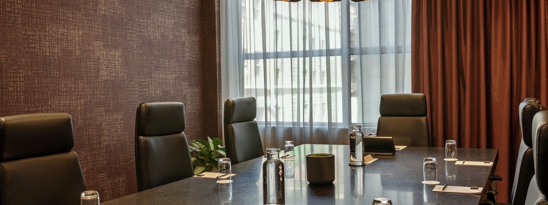Leather chairs by a long stone table under a circular light fixture in Salon Du Président at Warwick Le Crystal Montreal