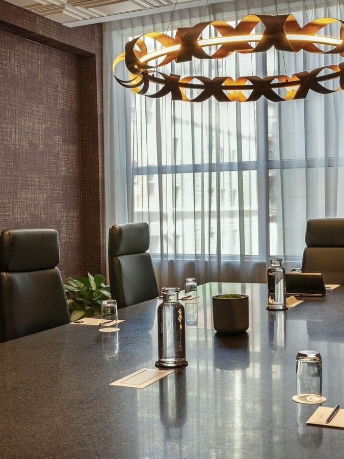 Leather chairs by a long stone table under a circular light fixture in Salon Du Président at Warwick Le Crystal Montreal