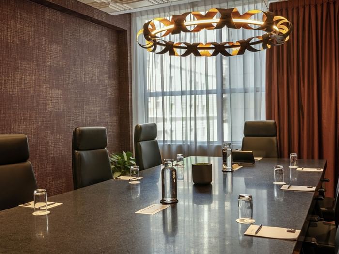 Leather chairs by a long stone table under a circular light fixture in Salon Du Président at Warwick Le Crystal Montreal