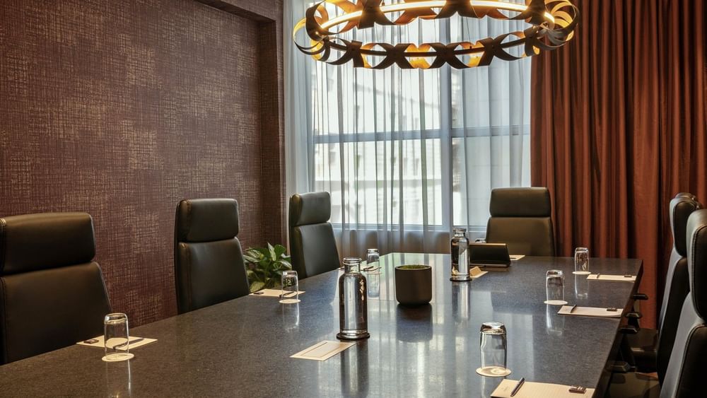 Leather chairs by a long stone table under a circular light fixture in Salon Du Président at Warwick Le Crystal Montreal